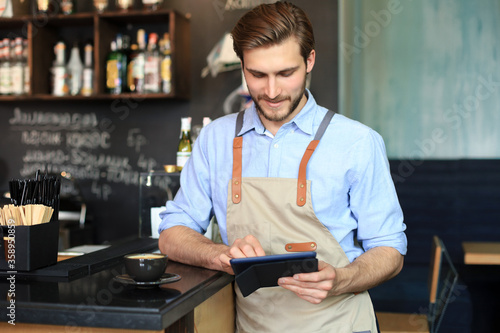 Young male owner using digital tablet while standing in cafe.