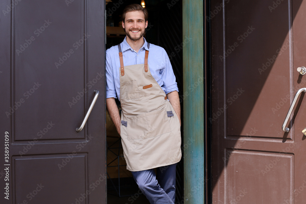 Handsome and confident cafe owner standing at the door. Young man looking at camera smiling. Handsome and confident cafe owner standing at the door. Young man looking at camera smiling.