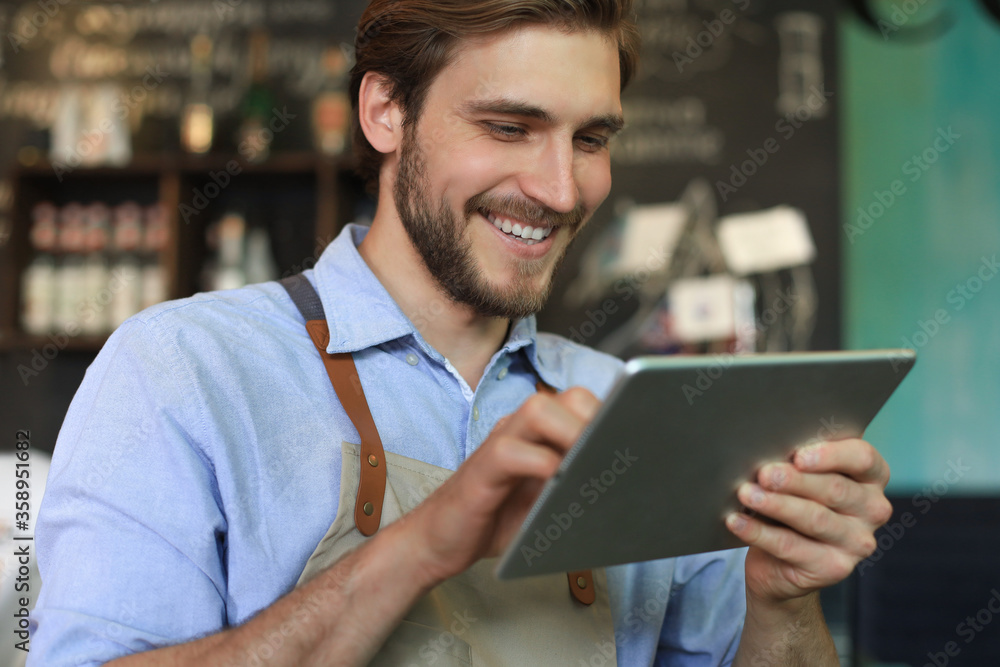 Young male owner using digital tablet while standing in cafe. Young male owner using digital tablet while standing in cafe.