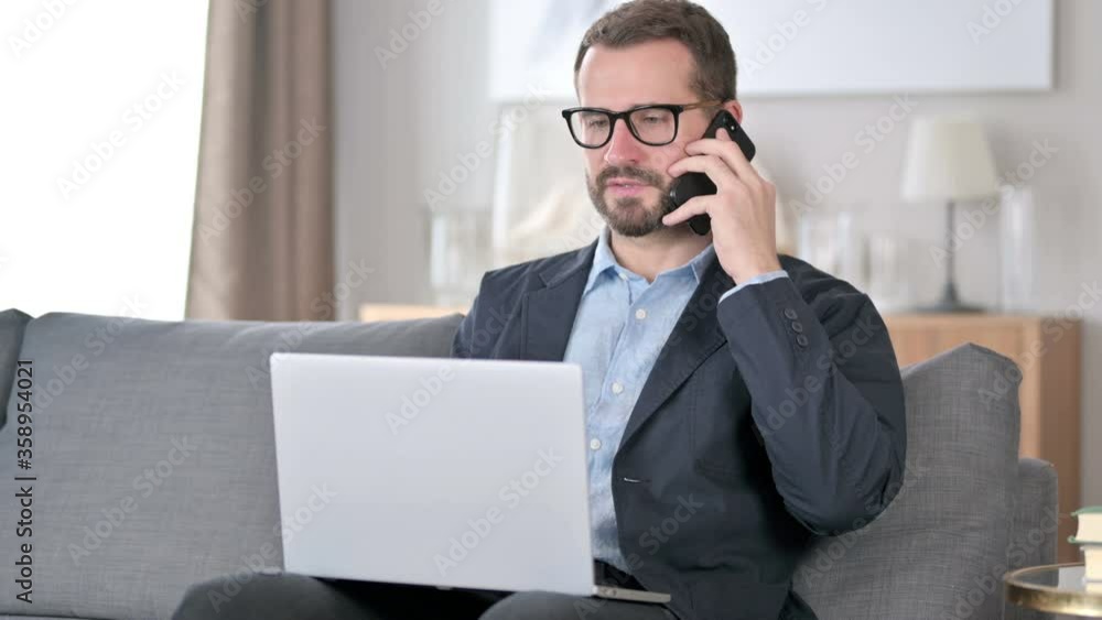 Young Businessman with Laptop Talking on Smartphone at Home Young Businessman with Laptop Talking on Smartphone at Home