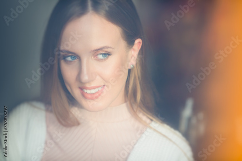 Portrait of a beautiful happy girl with light brown hair. Attractive young woman in a white sweater smiles and looks away. Tender and comfortable mood. Soft lighting.