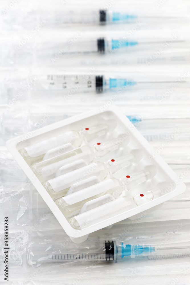 Closeup transparent glass ampoules with medicine in package on the packaging of disposable syringes. Shallow focus. Closeup transparent glass ampoules with medicine in package on the packaging of disposable syringes. Shallow focus.