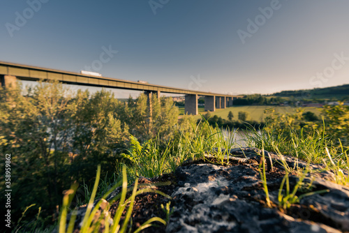 German Autobahn bridge in blurred background with natural foreground in focus for the highway A3 over the danube river near Regensburg with moving cars in golden afternoon light on clear summer day