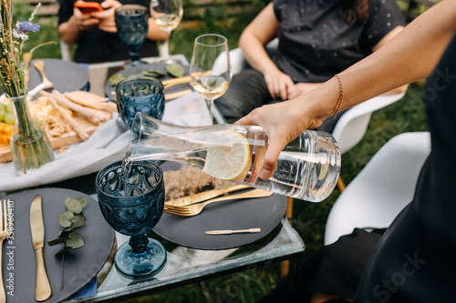 Female hand pouring still water with lemon in a glass at a party.