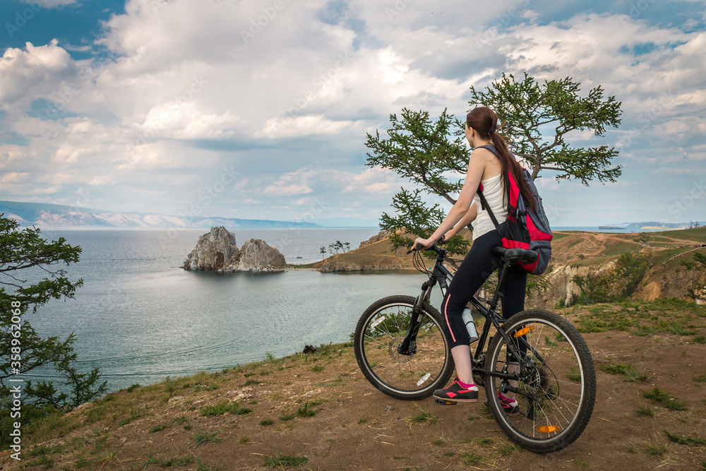 Fototapeta premium a girl travels on a bicycle with a backpack on Lake Baikal