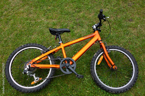 An orange children's Bicycle is lying on the green grass