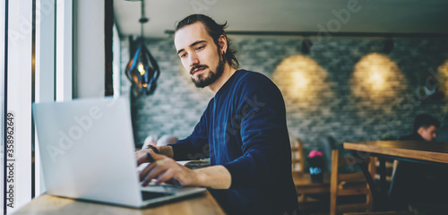 Caucasian student watching webinar on laptop computer improving skills on programming, serious professional web designer working on freelance sitting in cafeteria and using good wifi connection