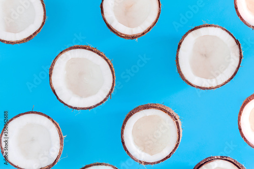 Brown halves of coconut nuts are scattered on blue background. Tropical palm fruit. Organic natural healthy vegan vegetarian meal, coco based food concept. Exotic pattern, backdrop, wallpaper.