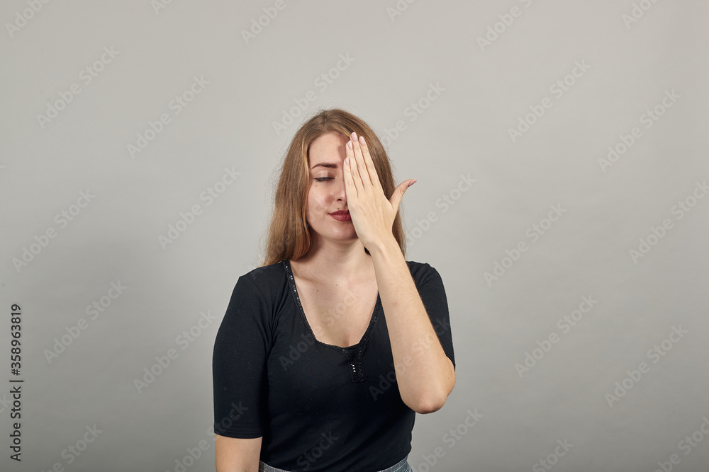 Closing face palms covers eyes visible through with hands. Young attractive woman, dressed black t-shirt, grey background Closing face palms covers eyes visible through with hands. Young attractive woman, dressed black t-shirt, grey background