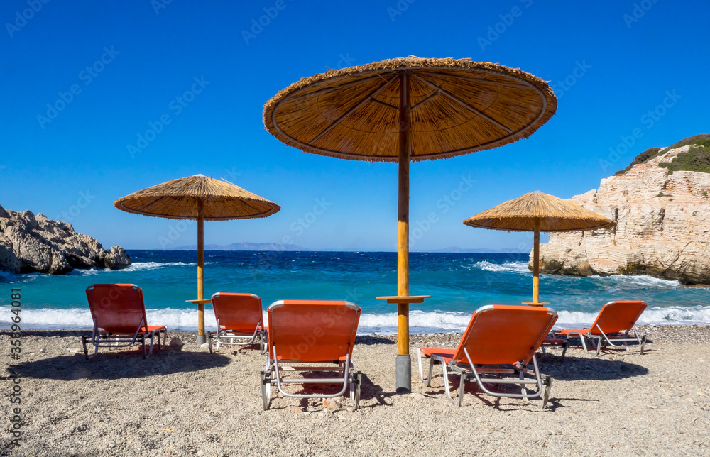 Summer beach without people in the 2020 season at the Mediterranean Sea. Beach landscape on the coast of Greece with sun beds and beach umbrellas at seashore.