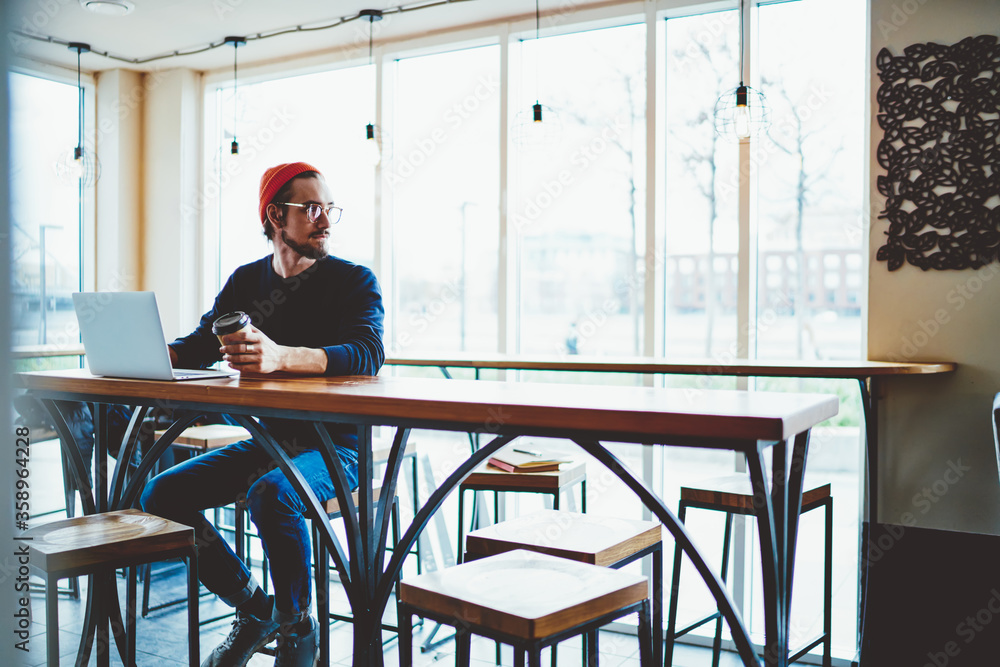 Fototapeta premium Pondering hipster guy thoughtful looking away and thinking about information database on laptop computer during distance job in coffee shop, Caucasian freelancer have freelance work on netbook