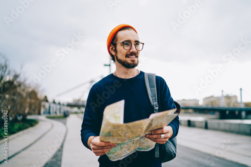 Obraz na płótnie Cheerful caucasian hipster guy in trendy spectacles satisfied with active vacation having trip , smiling male traveler strolling with map having city tour excited with urban setting on weekends