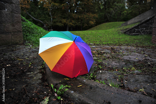Rainbow colored umbrella in park area.  The umbrella is placed in a circle of flat stones. Artillery battery from World War 2 visible.