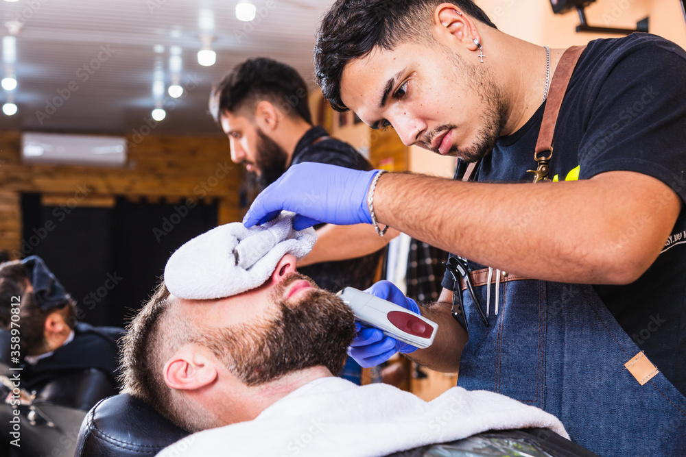 Fototapeta premium Two barbers working in a fancy barbershop. Bearded men enjoy the moment.