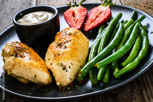 Roasted chicken fillets with green beans and strawberries on wooden table 