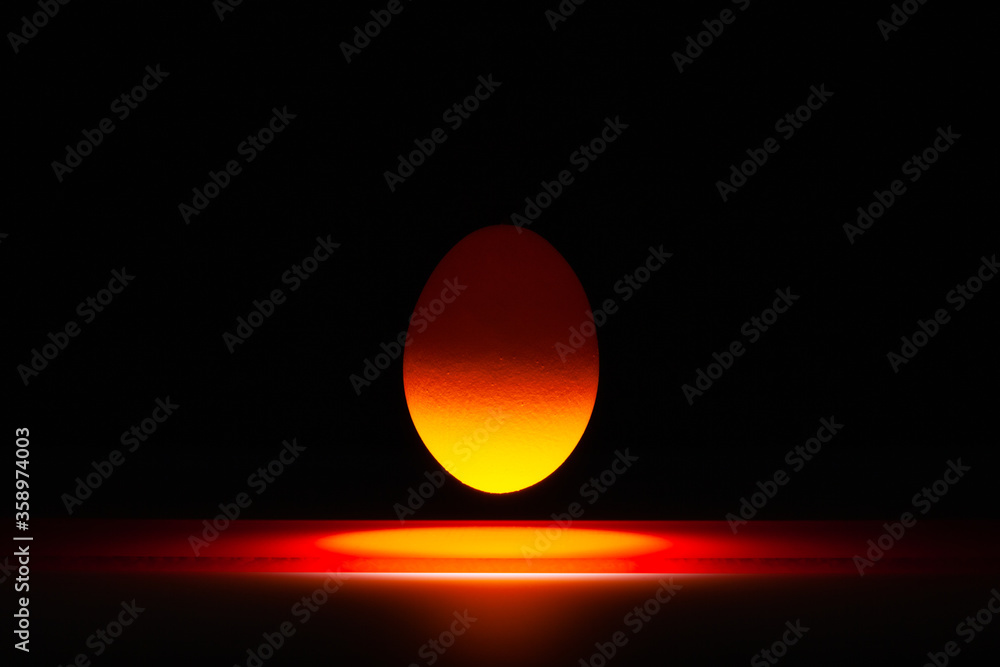 Orange egg levitating over a black glass table Orange egg levitating over a black glass table