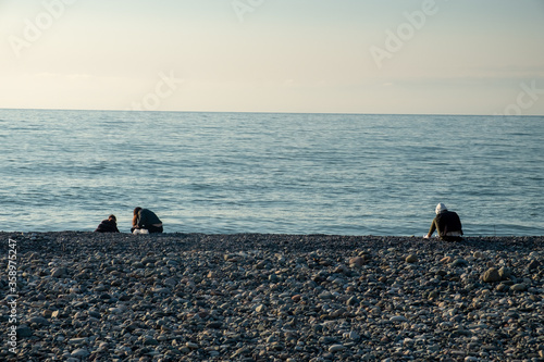 Silhouettes of people on the background of the sea and sunset. Solar path on the water. Small ripples ha surface of the water. Beach, a beach from a galois. Evening. Spring. Georgia. photo