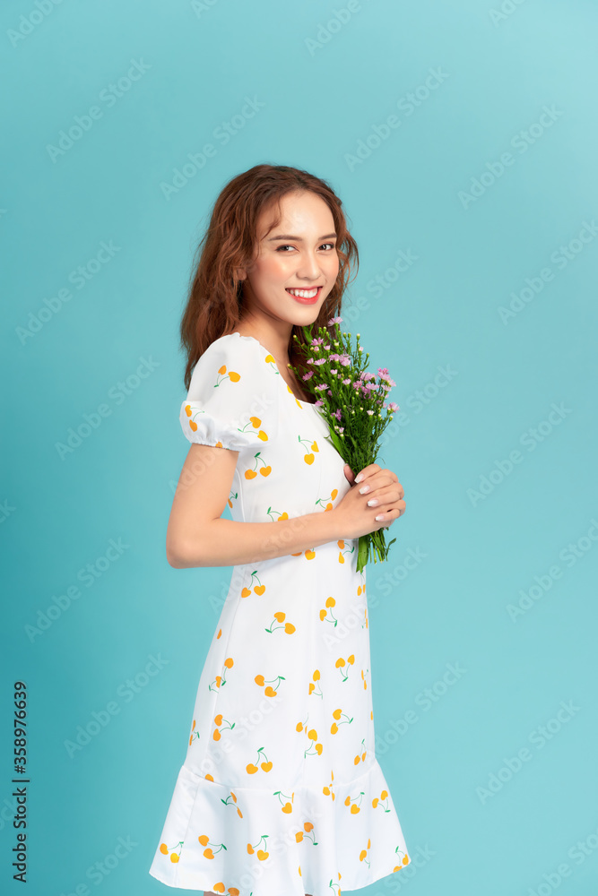Portrait of a cheerful pretty woman holding flowers over blue background