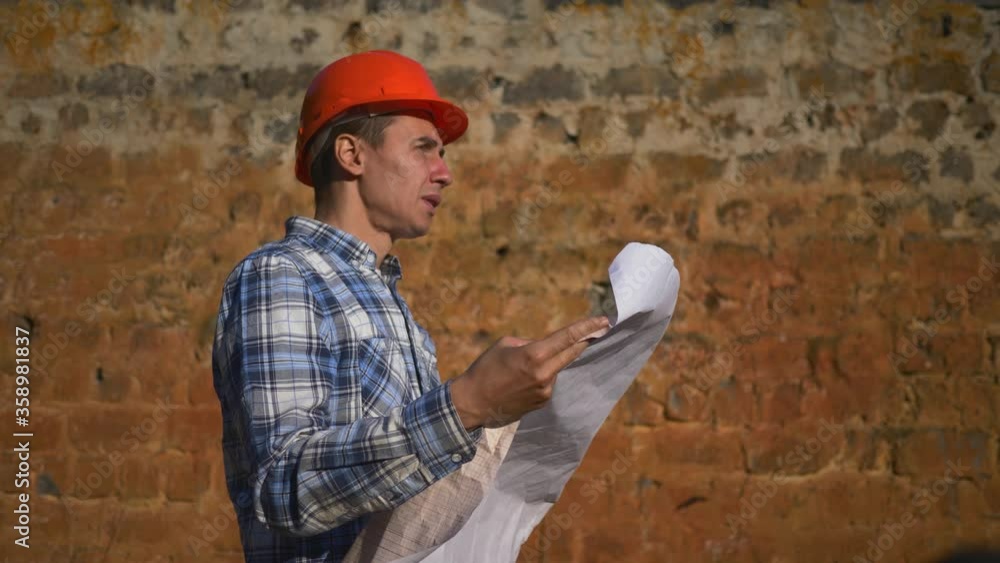 The Builder, foreman stands on the construction site and looks at the project of the building. The architect is working on a project to reconstruct an old brick building. The Builder, foreman stands on the construction site and looks at the project of the building. The architect is working on a project to reconstruct an old brick building.