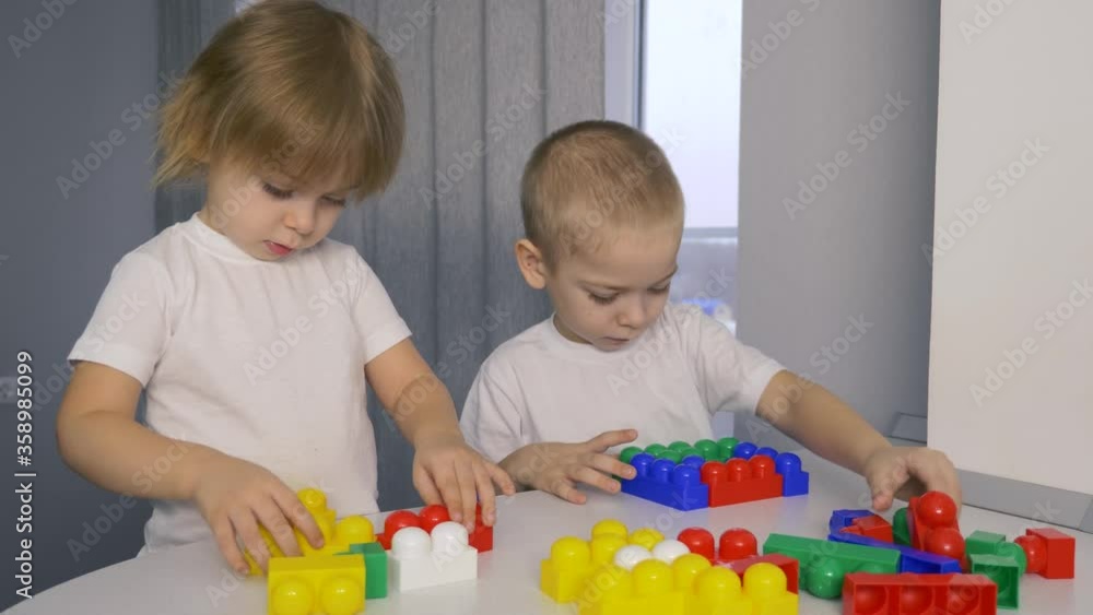 Happy children at home at the table build a house of colored cubes. P Happy children at home at the table build a house of colored cubes. P