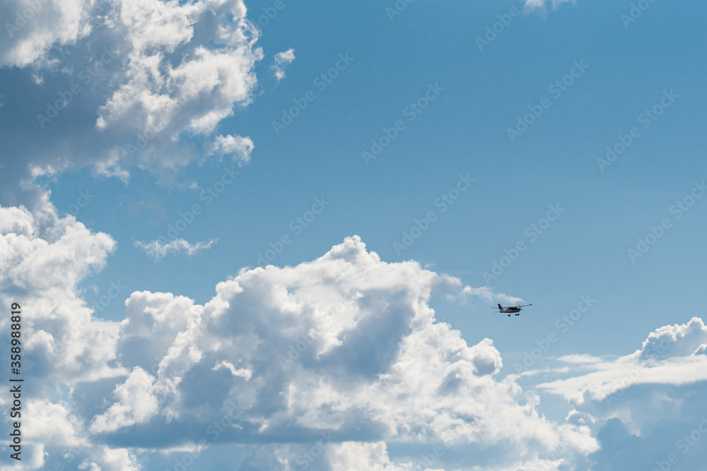 Fototapeta premium A small plane in front of giant clouds after the storm. The clouds break open and blue sky prevails.