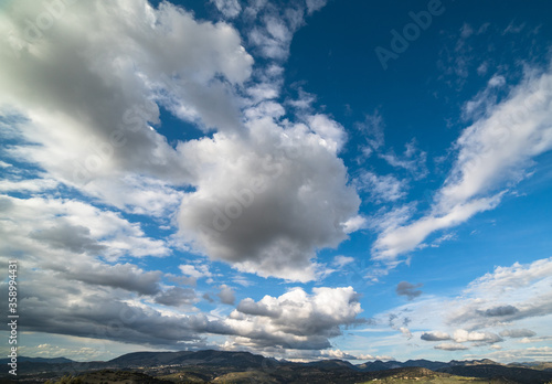 White clouds on blue sky above mountains.