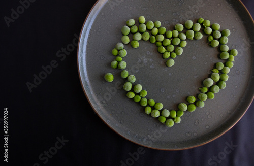 Heart of frozen green peas in a plate on a dark background.