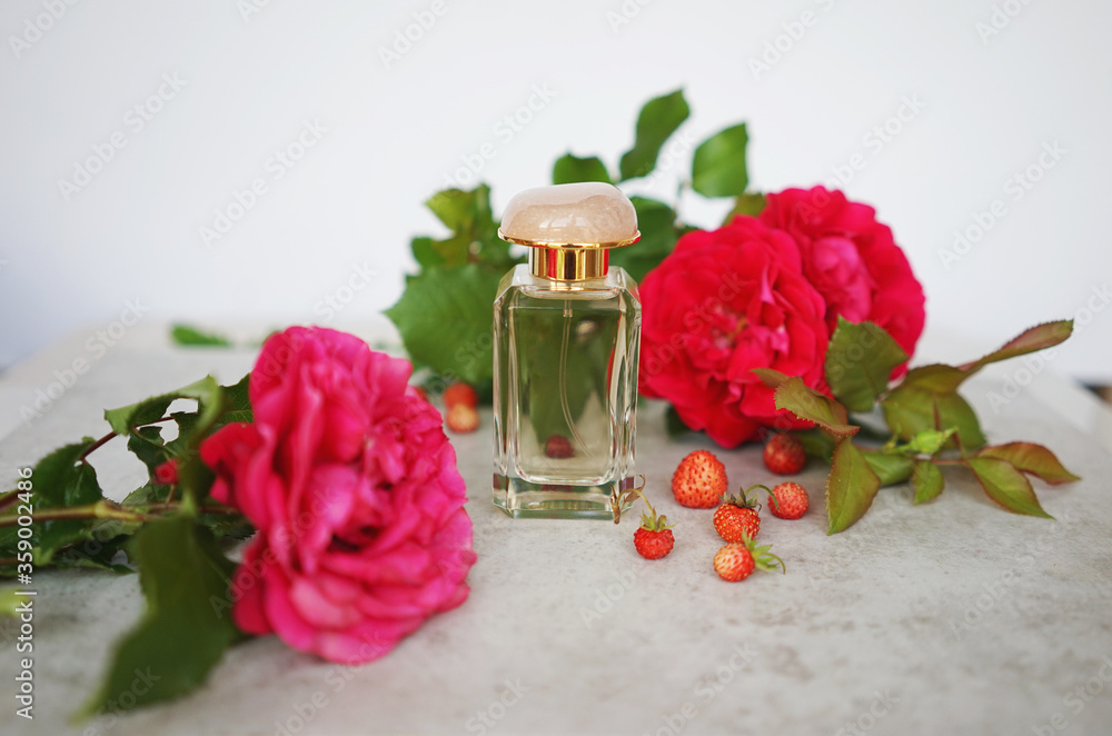 glass perfume bottle with wild strawberries and red roses. Concept of floral berry aroma glass perfume bottle with wild strawberries and red roses. Concept of floral berry aroma
