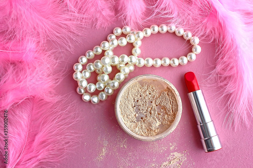 Loose make-up powder, light powder, white pearl necklace beads and boudoir in the dressing room pink retro lipstick in vintage style on a pink background and pink flamingo feathers