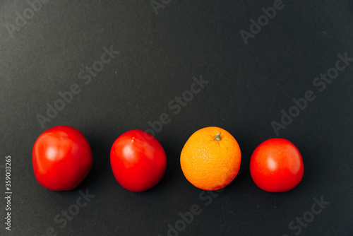 Orange and tomatoes in a row on a black background