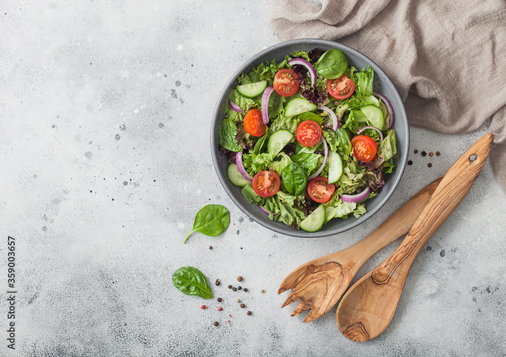 Spatula fork and spoon with bowl of healthy vegetarian vegetables salad with tomatoes and cucumber, lettuce and spinach on light background. Spatula fork and spoon with bowl of healthy vegetarian vegetables salad with tomatoes and cucumber, lettuce and spinach on light background.