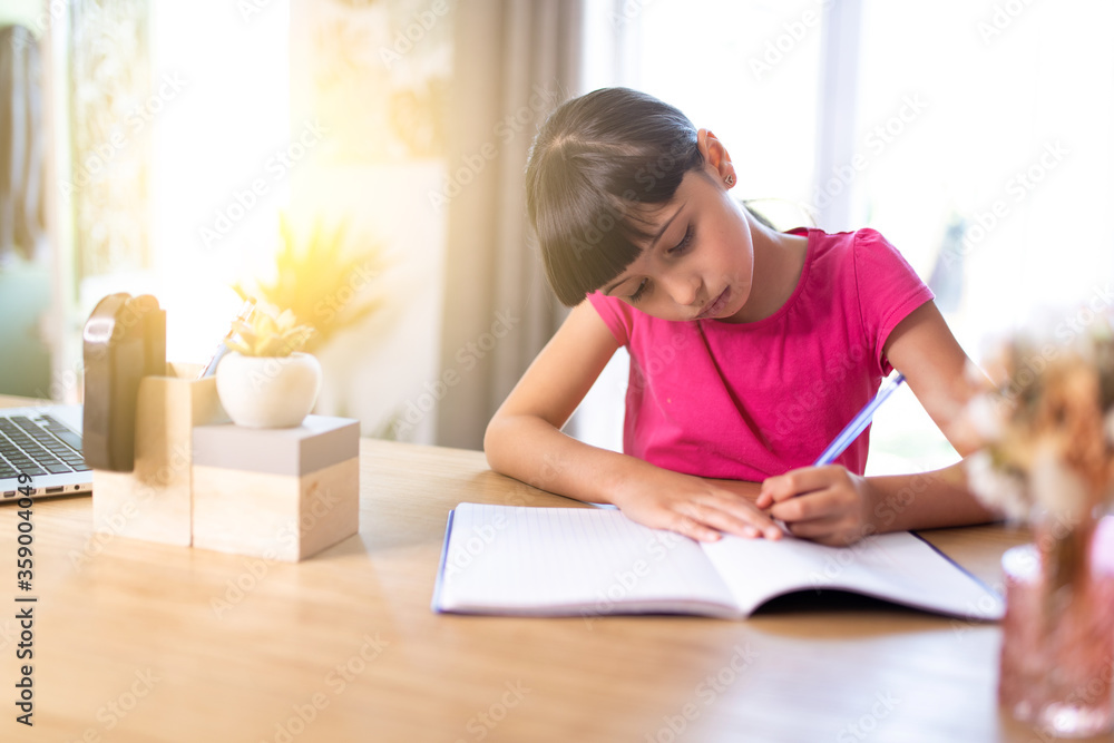 girl working studiously at home, writing with her left hand on a homework notebook girl working studiously at home, writing with her left hand on a homework notebook