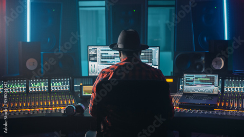 Stylish Artist, Musician, Audio Engineer, Producer Takes Place at His Control Desk in Music Record Studio, Uses Computer Screen show User Interface of DAW Software with Song Playing. Back View