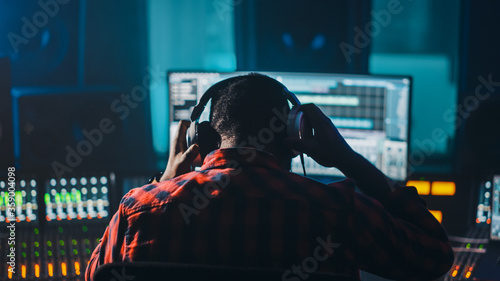 Photos Stylish Artist, Musician, Audio Engineer, Producer Takes Place at His Control Desk in Music Record Studio, Uses Computer Screen show User Interface of DAW Software with Song Playing