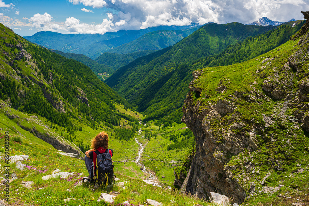 Woman with backpack resting on mountain top, looking at view dramatic landscape valley summer activity fitness wellbeing freedom concept, rear view