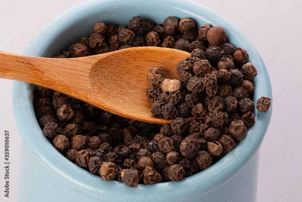 black pepper in a clay pot with a wooden spoon, isolated on a white background