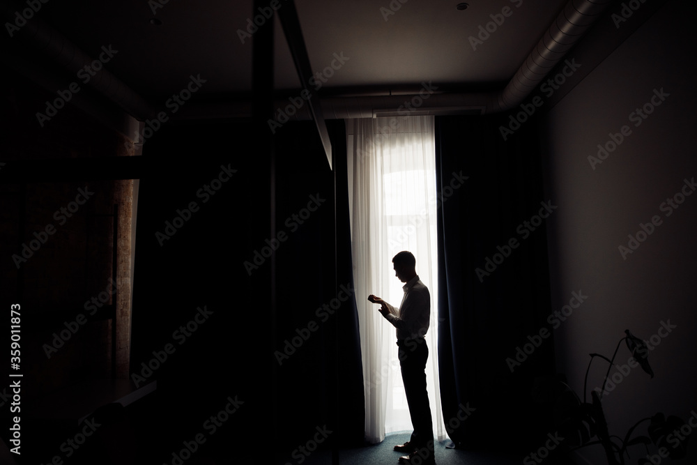 Handsome brutal groom in blue suit near the window