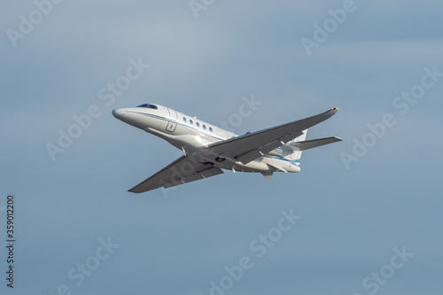 White small turbofan-powered business jet airplane flying in the air after takeoff from airport. Fast modern aircraft for air transportation. Aviation technology. Travel and business concept.
