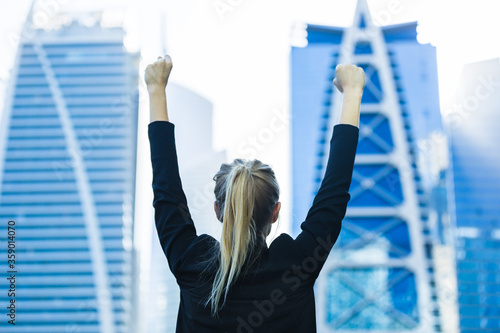 Business success - Passionate young businesswoman celebrating overlooking the city center high-rises with both arms raised.
