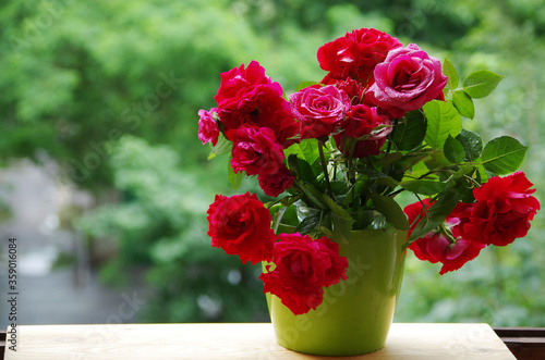 Fototapeta Naklejka Na Ścianę i Meble -  A bouquet of red roses in a green vase standing on a windowsill.