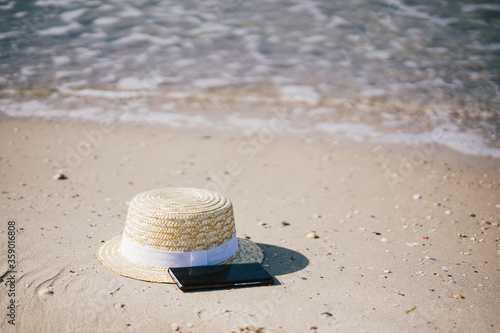 straw hat with a phone on the sand near the sea 