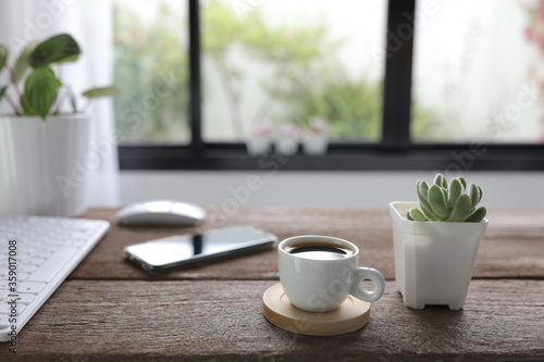 White coffee cup with mouse and keyboard and phone with small succulent plant on rustic wooden dinning table interior home