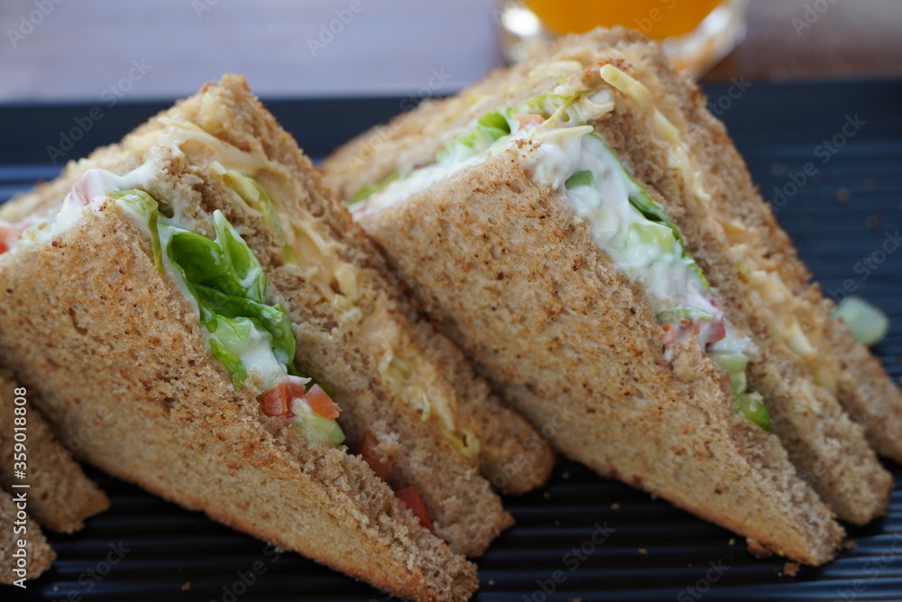 Two club sandwiches placed on a black plate at a restaurant. Close-up photo of a club sandwich. Sandwich with prosciutto, vegetables, lettuce and mayo on a fresh sliced rye bread on wooden background.