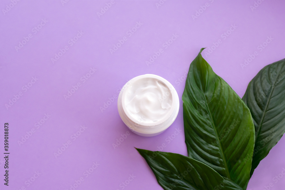 Soft white cream in jar with bright green leaves on purple background with copy space. Spa treatment and procedure at home. Soft white cream in jar with bright green leaves on purple background with copy space. Spa treatment and procedure at home.