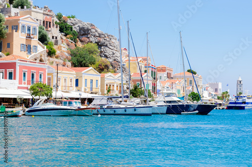 Wonderful view on colorful houses on rocks and sailing boats near the deep blue Mediterranian sea on Greek island Symi in sunny summer day, holidays on exotic islands