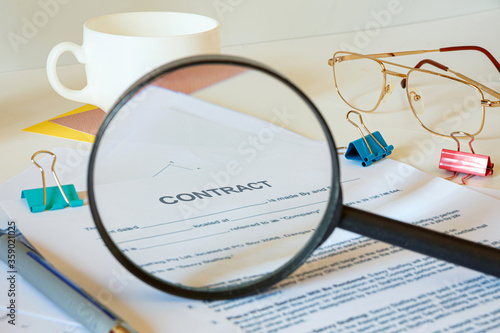 Desktop office desk, notebook, glasses, pen and documents. Magnifier approximates the word CONTRACT photo