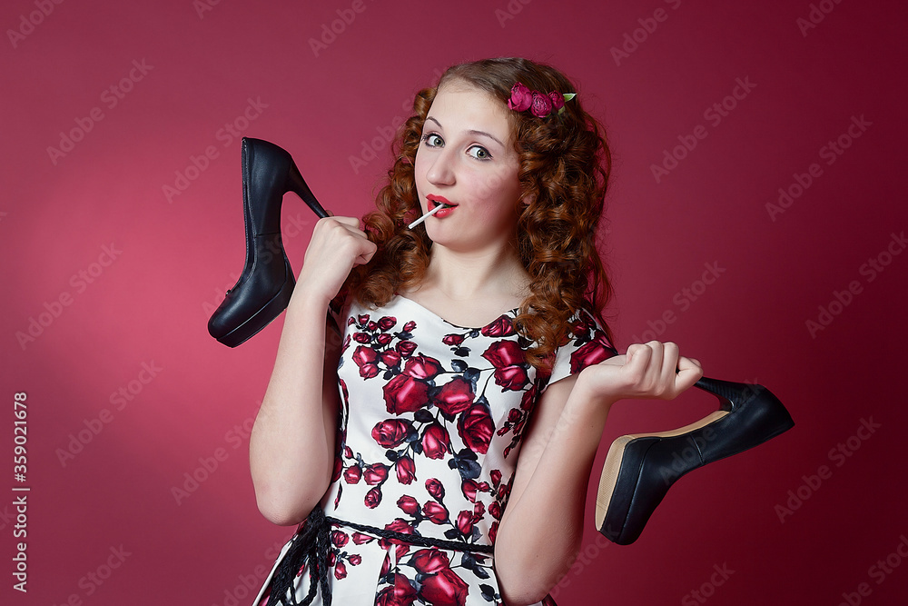 Portrait of a cute girl in pin-up style with shoes in hand on red paper background. Stylish photography in vintage style. Portrait of a cute girl in pin-up style with shoes in hand on red paper background. Stylish photography in vintage style.