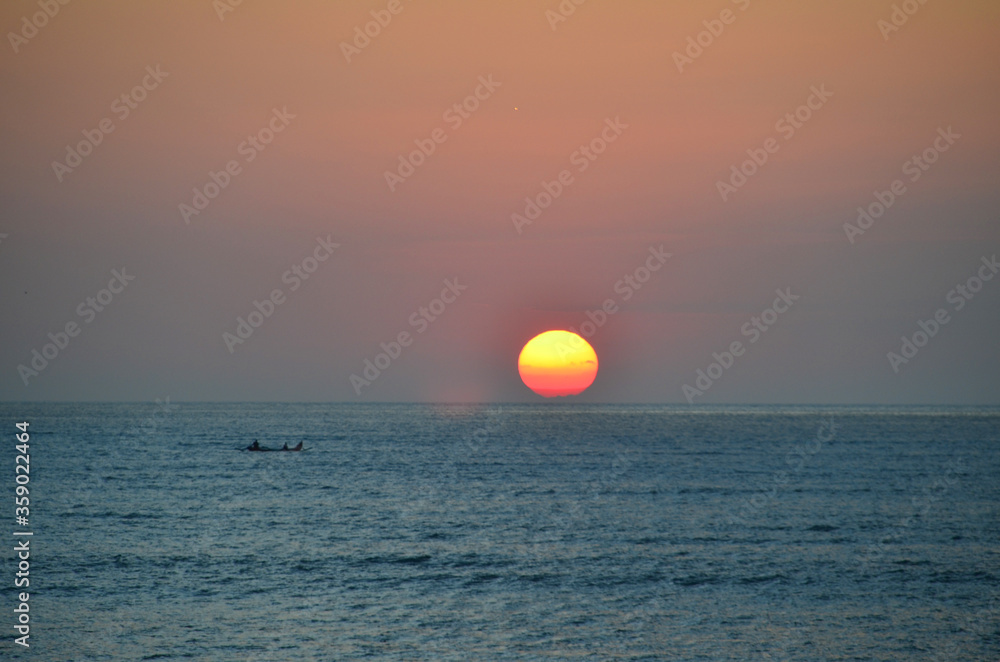 Beautiful sunset with a sailing boat at Jimbaran beach. Jimbaran is a fishing village and tourist resort in Bali, Indonesia.