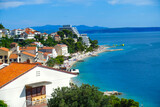 Podgora Chorwacja widok na panoramę miasta, promenadę, plażę, morze Adriatyckie, w tle góry Biokovo. Lazur wody i błękit nieba.