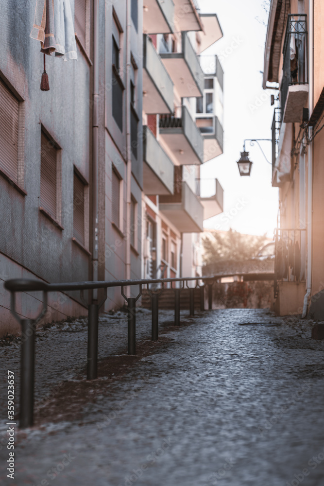 Fototapeta premium Vertical shot with a shallow depth of field of a typical sloping narrow street of Portugal with a metal banister, paving-stone on the ground facades of residential houses with closed windows on sides